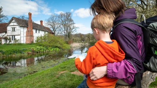 A mother and child sit on a bench overlooking the manor house.